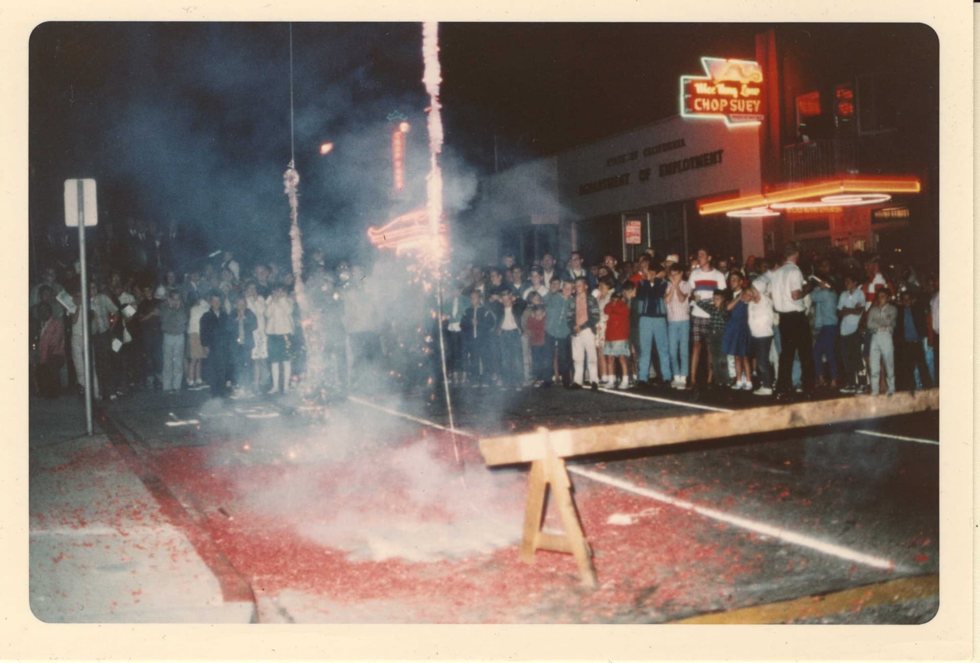 People celebrating in front of Mee Heng Low Noodle House with fireworks in the background